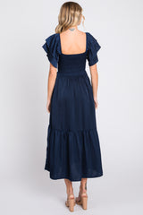 woman wearing a navy blue midi dress with short flutter sleeves and a smocked bodice, viewed from the back