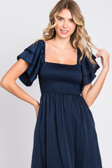 woman wearing a navy blue dress with a square neckline and ruffled short sleeves.