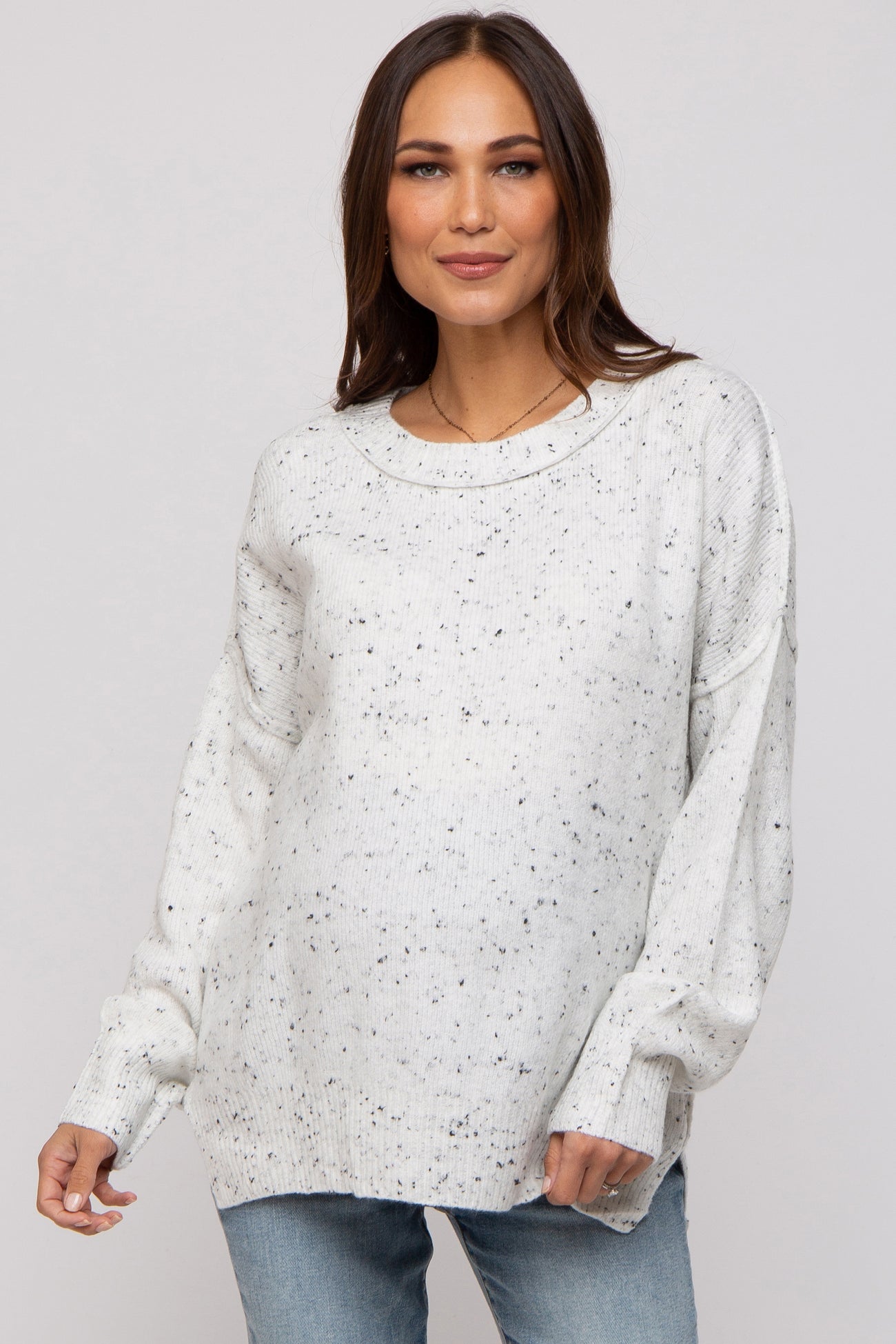 woman wearing a light grey speckled maternity sweater with a relaxed fit and long sleeves, showing her baby bump
