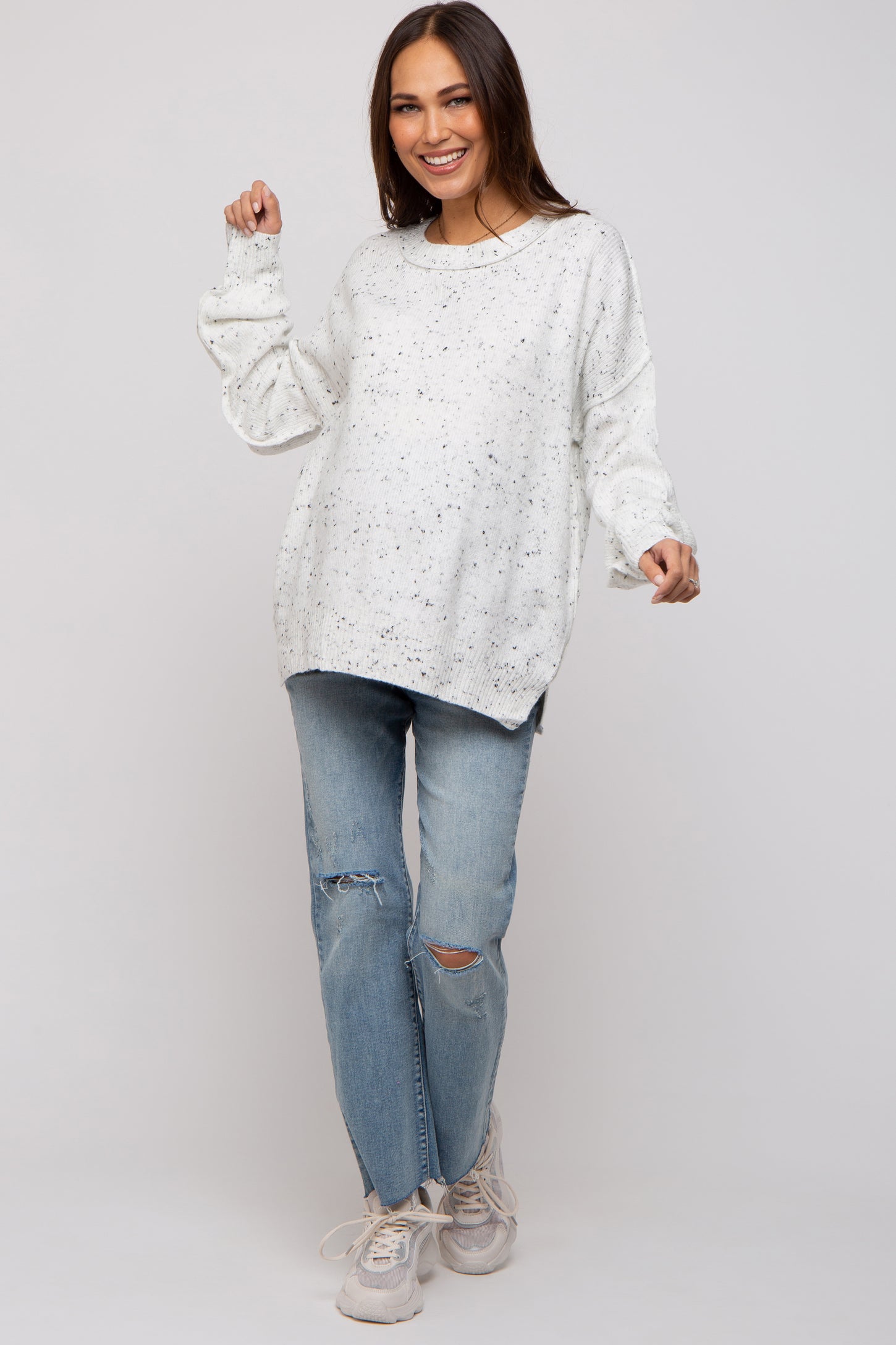 woman wearing a white speckled oversized maternity sweater with relaxed fit and paired with distressed light wash jeans