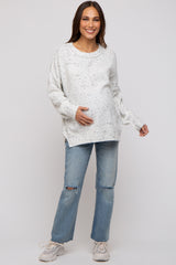 woman wearing a white speckled maternity sweater and distressed jeans, holding her baby bump