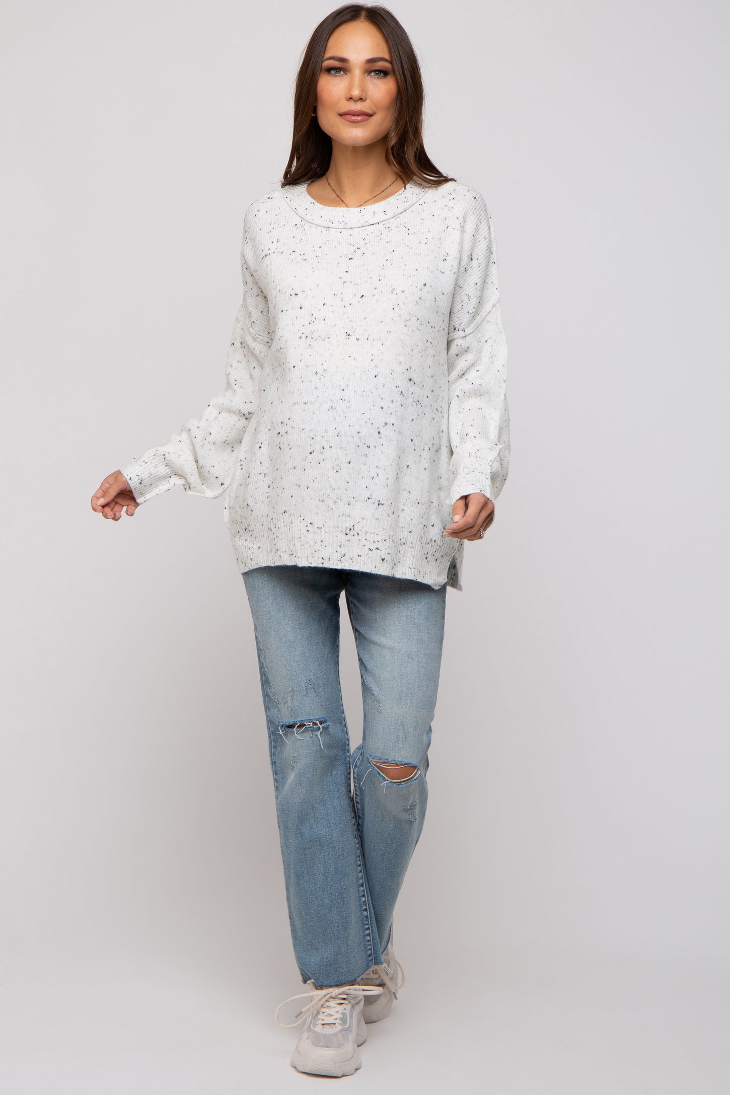 woman wearing a white speckled maternity sweater with long sleeves and paired with distressed light blue jeans