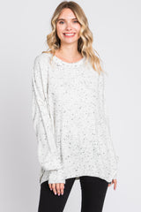 woman wearing a light gray oversized sweater with a speckled design and long sleeves, styled with black pants
