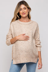woman wearing a beige maternity sweater with speckled details and holding her baby bump