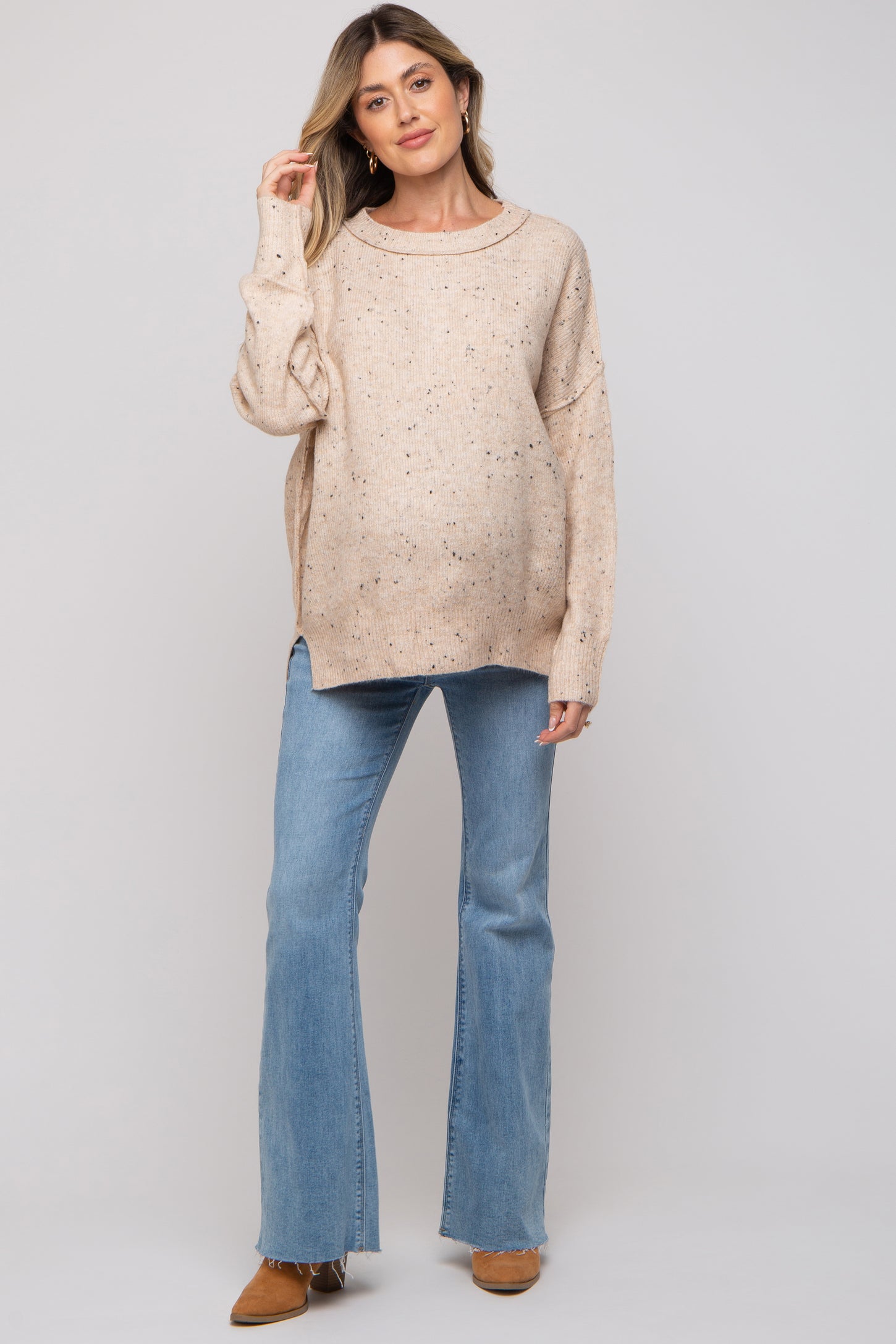 woman wearing a beige maternity sweater with speckled details and blue flared jeans, showing her baby bump