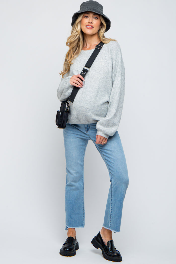 woman wearing a gray oversized sweater and light blue jeans with a baby bump, accessorized with a black bucket hat and bag