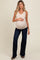 woman wearing a beige maternity tank top and dark blue flared jeans, showing her baby bump