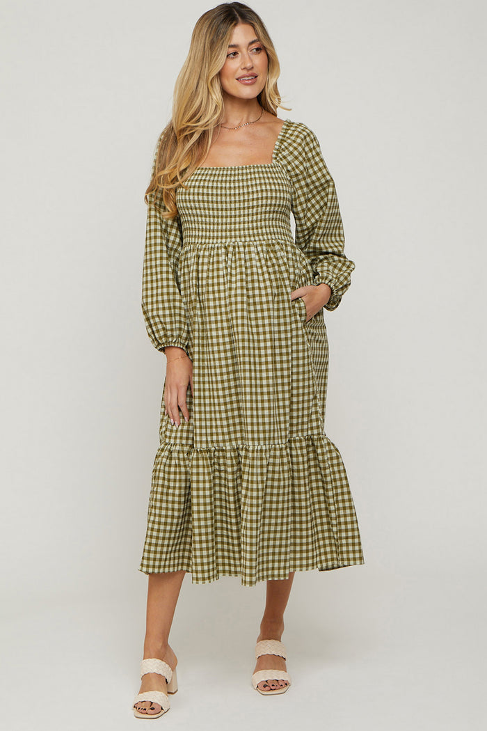 woman wearing a green and white checkered maternity dress with puff sleeves and a tiered hem, smiling at the camera