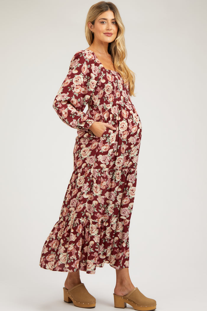 woman wearing a burgundy floral maternity maxi dress with long sleeves and pockets, showing her baby bump