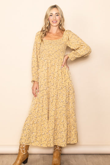 woman wearing a mustard yellow floral print long sleeve maxi dress with a smocked bodice and tiered skirt