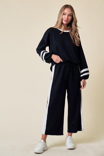 woman wearing a black lounge set with white stripes, featuring a loose top and wide-leg pants, standing against a neutral background