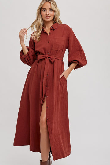 woman wearing a rust-colored long sleeve button-up dress with a belted waist and pockets