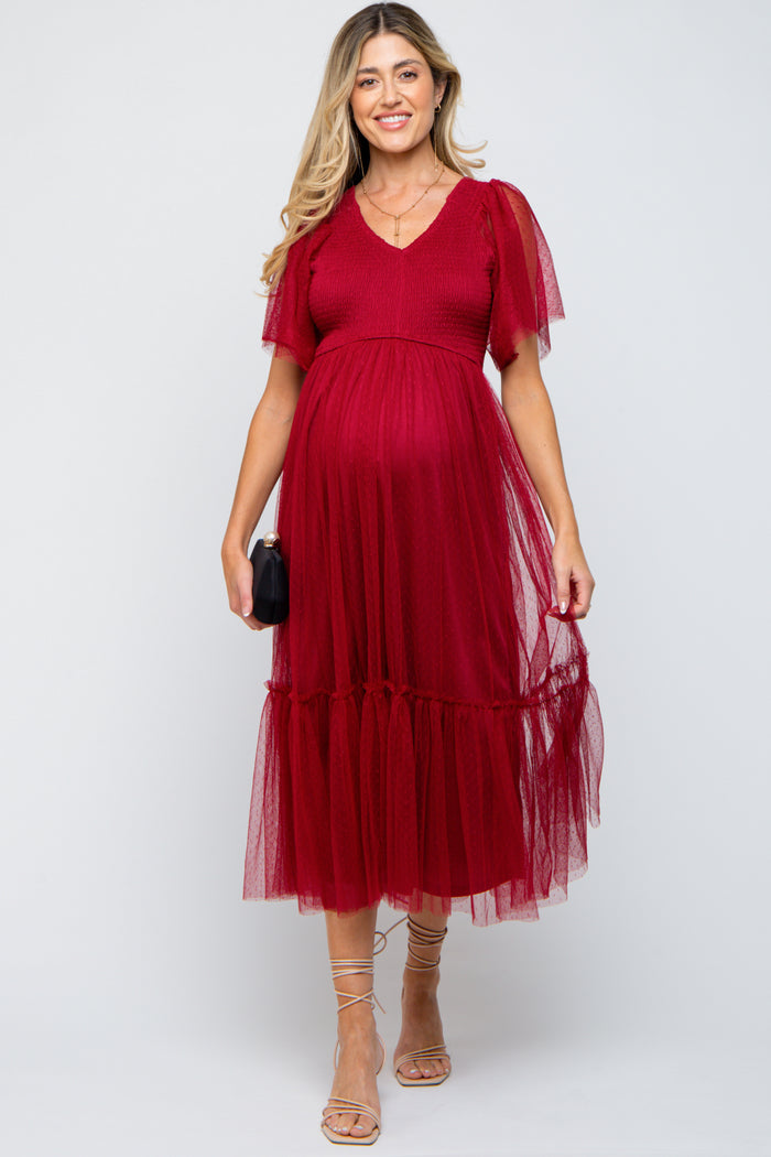 woman wearing a red maternity dress with ruffle sleeves and a layered tulle skirt, showcasing her baby bump