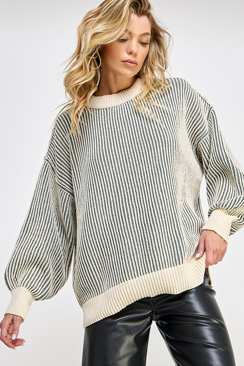 woman wearing a cream striped oversized knit sweater with balloon sleeves and a relaxed fit, paired with black leather pants