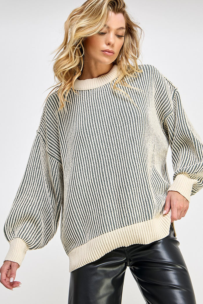 woman wearing a cream striped oversized knit sweater with balloon sleeves and a relaxed fit, paired with black leather pants
