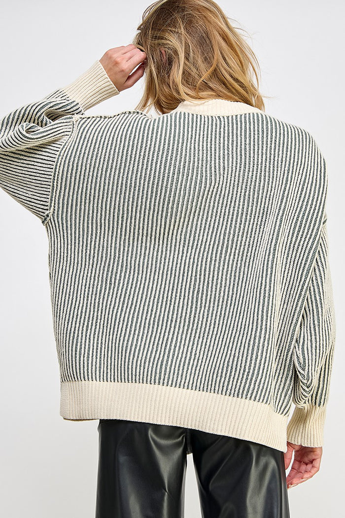 woman wearing a light striped oversized sweater in cream and grey with ribbed details, viewed from the back