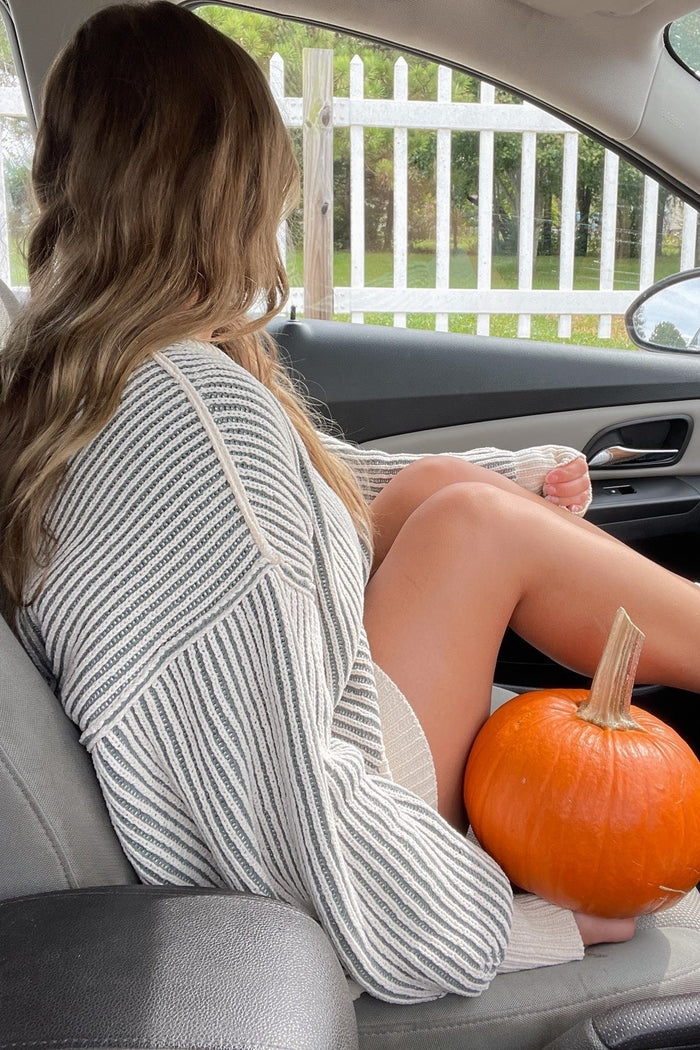 woman sitting in a car wearing a cream and gray striped oversized sweater, holding a pumpkin on her lap