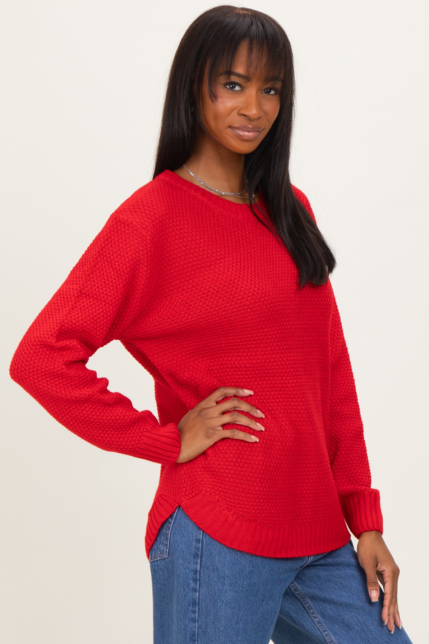 woman wearing a red textured knit sweater with side slit details and long sleeves, paired with blue jeans