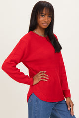 woman wearing a red textured knit sweater with side slit details and long sleeves, paired with blue jeans