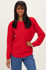 woman wearing a red textured sweater paired with blue jeans, smiling at the camera