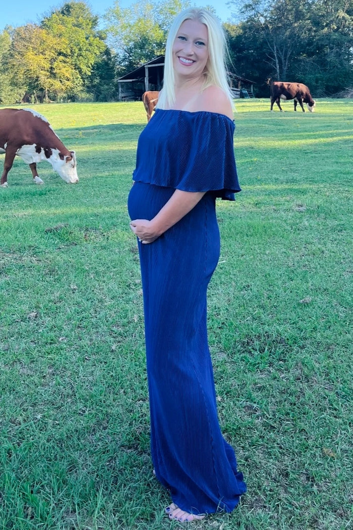 woman wearing a navy off-shoulder maternity dress and showing her baby bump in a grassy field with cows in the background