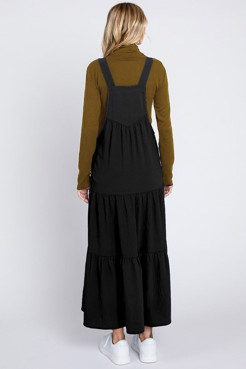 woman wearing a black tiered maxi dress over a long sleeve olive green top and white sneakers, viewed from the back
