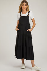 woman wearing a black maternity dress with a tiered design, buttons, and side pockets, styled with a white t-shirt and sneakers