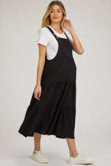 woman wearing a black maternity maxi dress with tiered layers and adjustable buttons, showing her baby bump.
