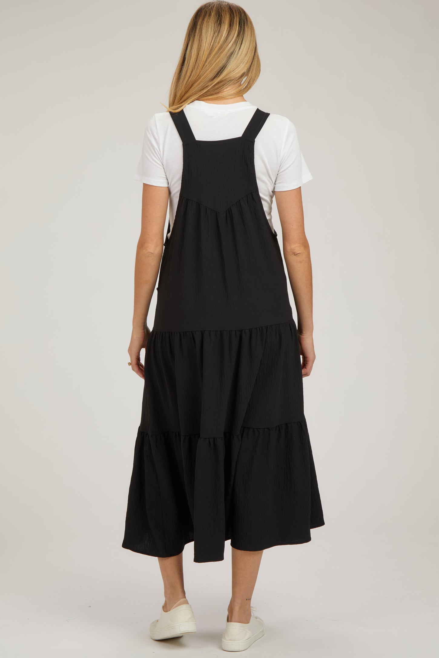 woman wearing a black maternity dress with a tiered skirt and adjustable straps, shown from the back