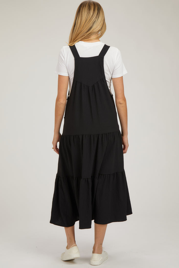 woman wearing a black maternity dress with a tiered skirt and adjustable straps, shown from the back