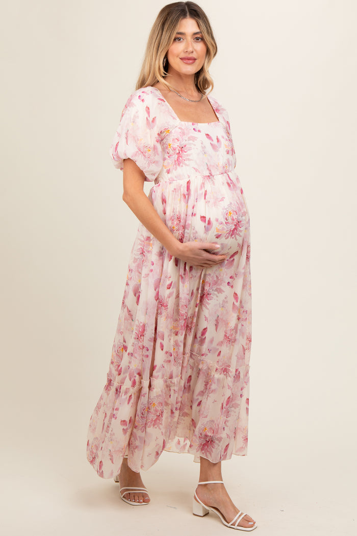 woman wearing a floral pink maternity maxi dress with puff sleeves and holding her baby bump