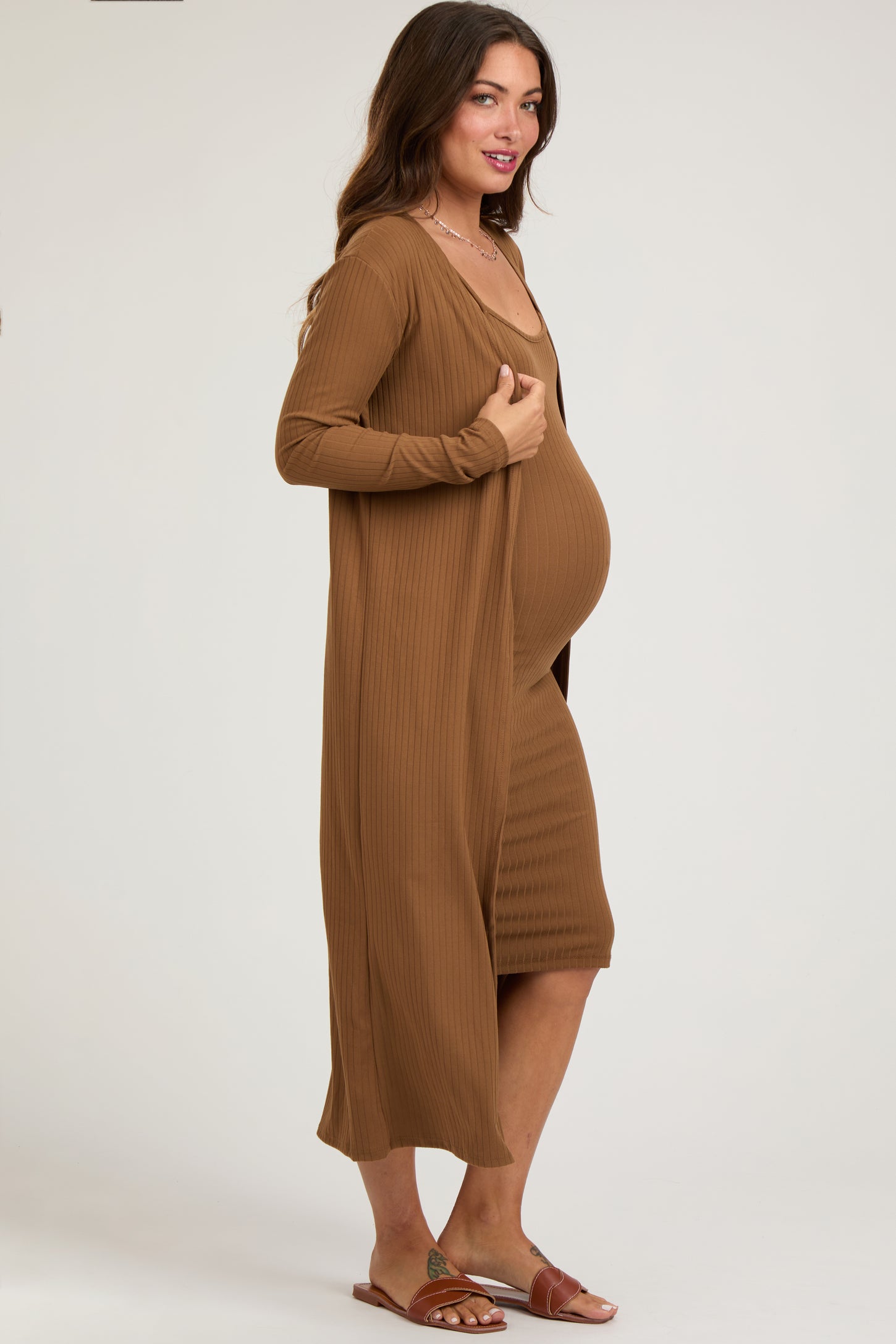woman wearing a brown ribbed maternity dress with a matching long cardigan and showing her baby bump