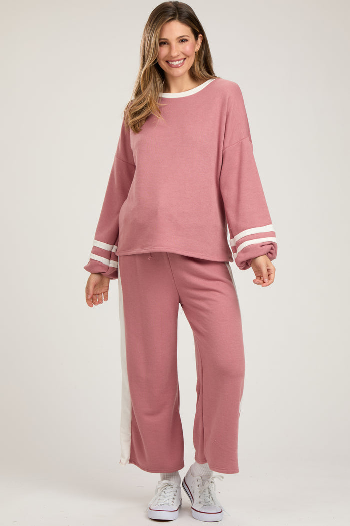 woman wearing a pink maternity loungewear set with white stripe details and wide sleeves, showcasing her baby bump