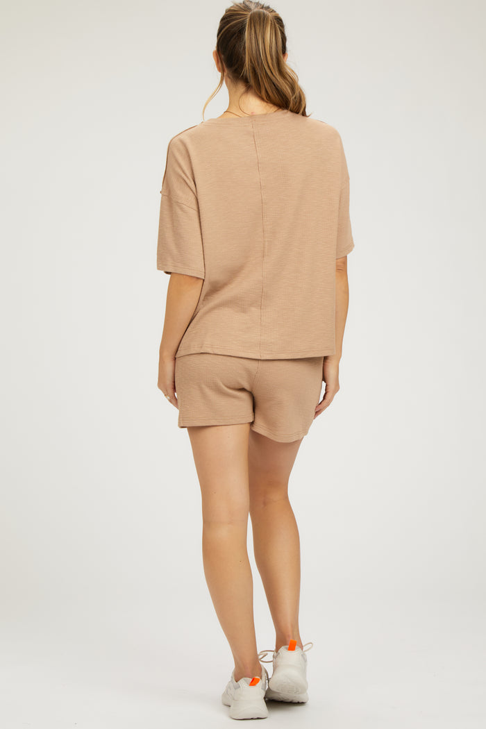woman wearing a beige maternity loungewear set with a short sleeve top and shorts, showing a comfortable back view