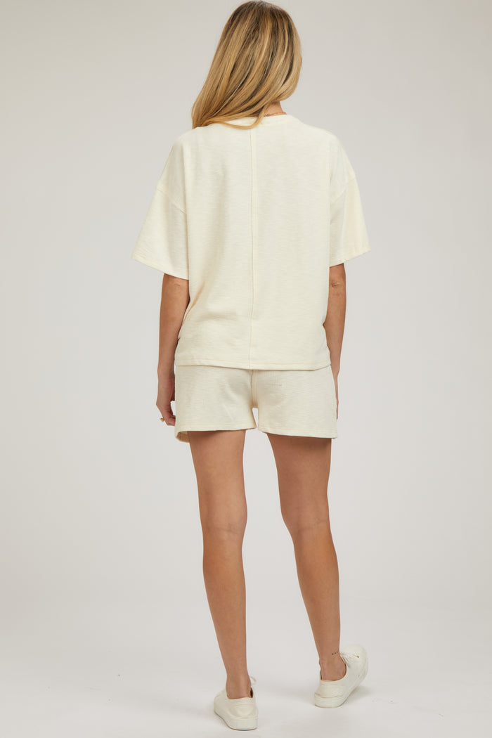 woman wearing a light cream maternity loungewear set, consisting of a short-sleeve top and shorts, with a relaxed fit