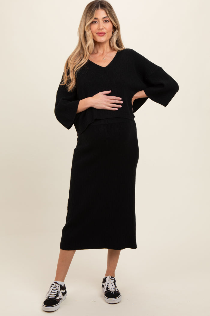 woman wearing a black maternity two-piece outfit with a v-neck top and a midi skirt, holding her baby bump