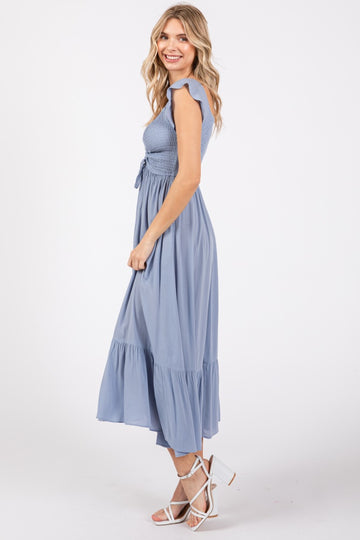 woman wearing a light blue smocked maxi dress with flutter sleeves and a tiered skirt, standing in profile