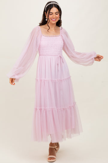 woman wearing a light pink tiered tulle maxi dress with long sleeves and a square neckline