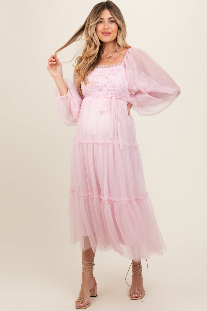 woman wearing a light pink maternity dress with puff sleeves and tiered skirt, showcasing her baby bump