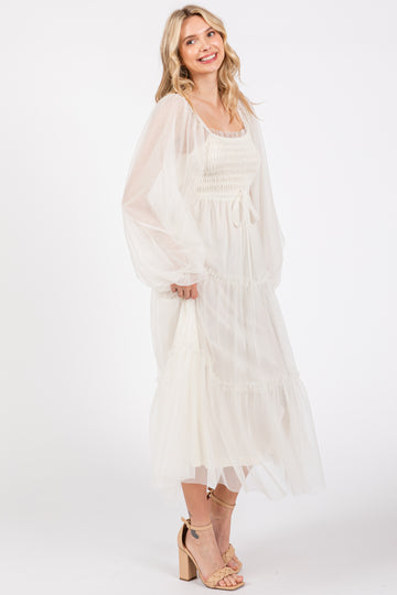 woman wearing a white smocked midi dress with sheer sleeves and a tiered skirt, smiling and standing sideways