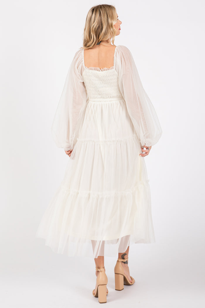 woman wearing a cream tiered midi dress with sheer puff sleeves and a smocked bodice, seen from the back