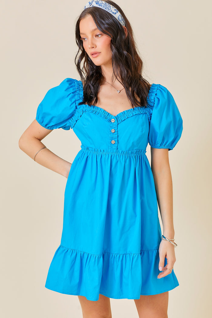 woman wearing a bright blue puff sleeve mini dress with a ruffled hem and button details