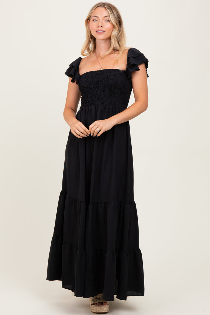 woman wearing a black strapless maxi dress with ruffled sleeves and a tiered skirt
