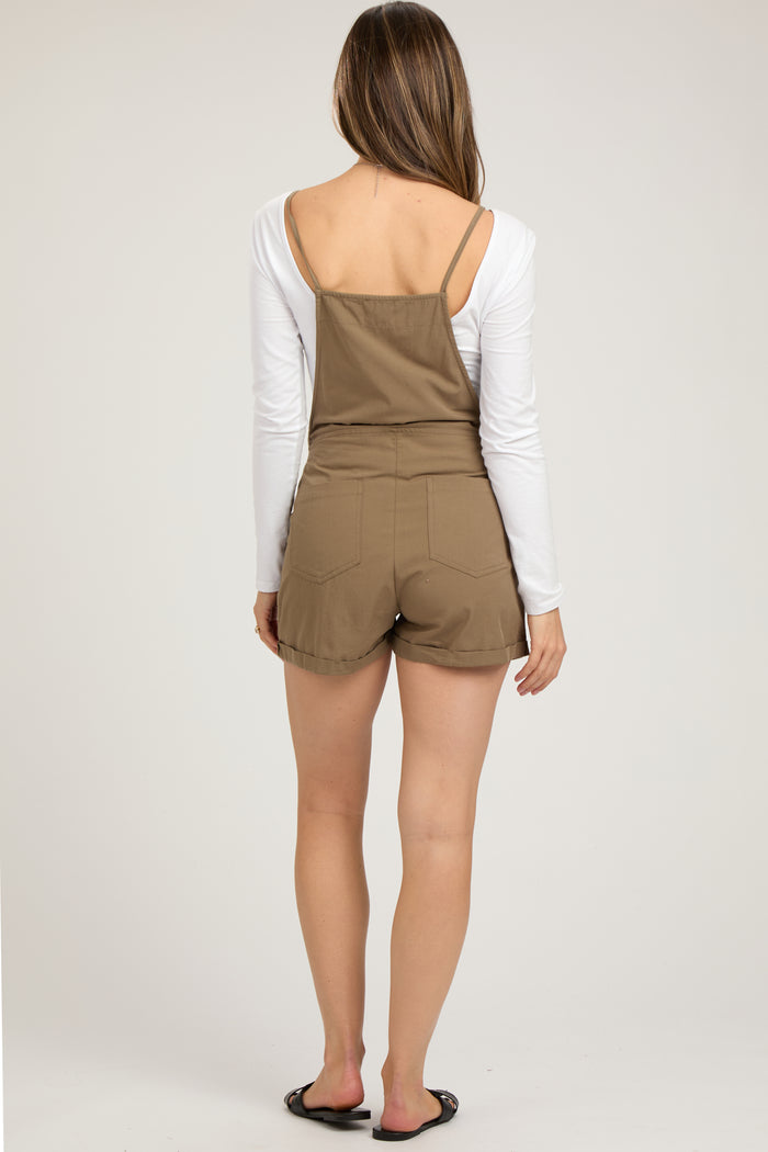 woman wearing a brown maternity overall shorts jumpsuit with a white long sleeve top, styled casually