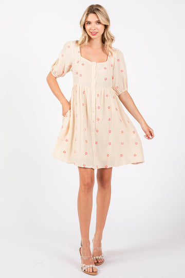 woman wearing a cream short sleeve dress with floral embroidery and a square neckline, standing and smiling