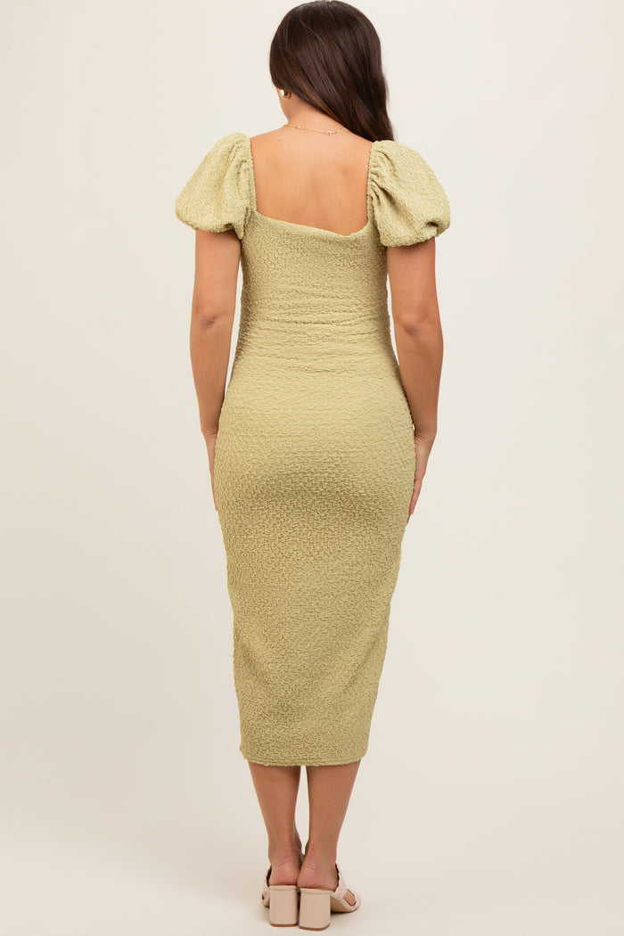 woman wearing a light green maternity dress with puff sleeves and a form-fitting silhouette, showing her baby bump from the back
