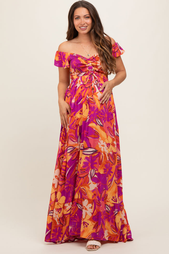 woman wearing a colorful off-shoulder floral maternity maxi dress with a gathered bodice and flowing skirt, highlighting her baby bump