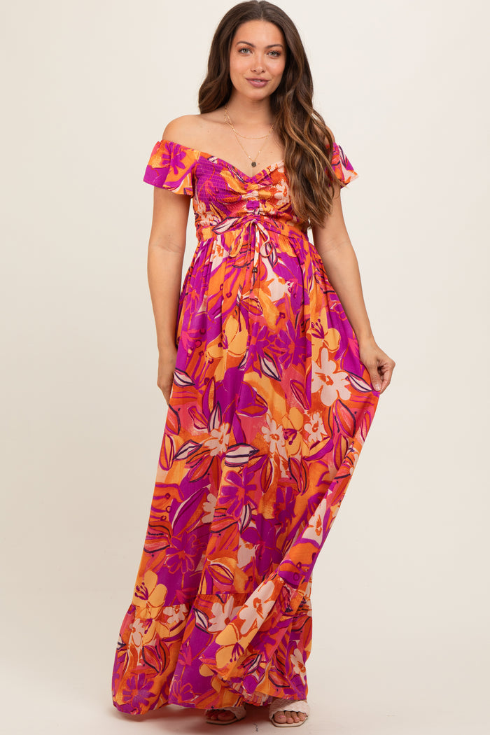 woman wearing a vibrant floral off-the-shoulder maxi maternity dress with a gathered bust and flowing skirt