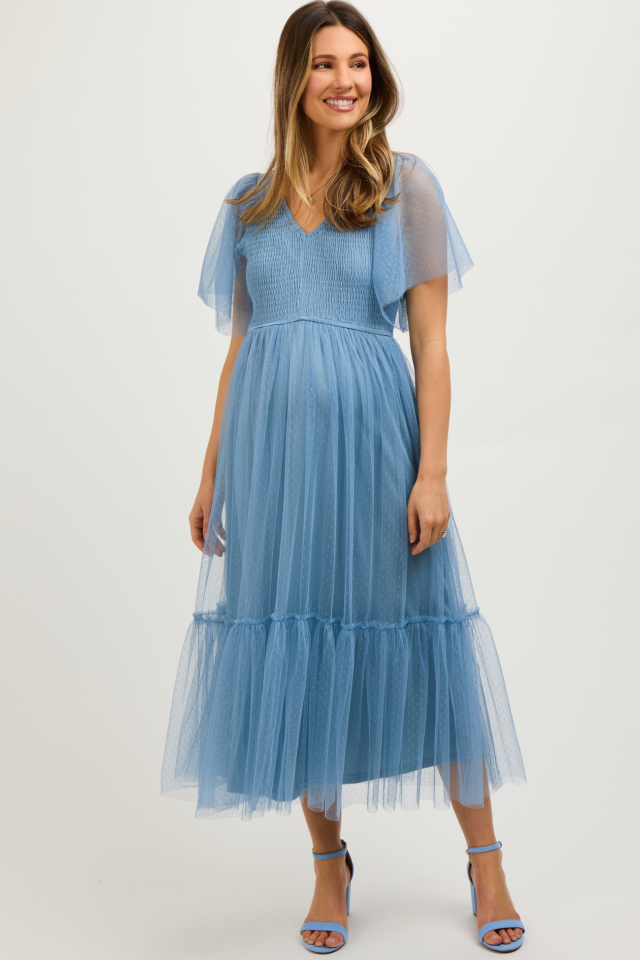 woman wearing a light blue maternity dress with sheer flutter sleeves and tiered tulle skirt, showing her baby bump
