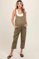 woman wearing a light olive green maternity jumpsuit with buttons and side pockets, showing her baby bump